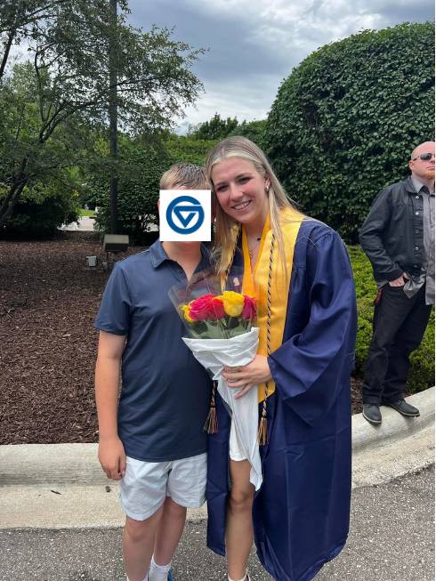 Julia Wood smiling in a blue gown. On the left, another individual stands nearby with a GVSU logo hiding their face.